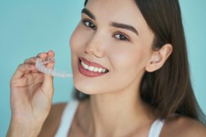 Woman holding clear Invisalign aligner and smiling against blue background.