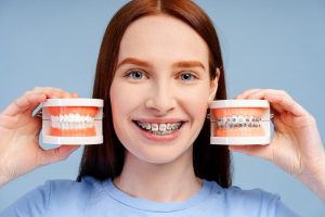 Smiling patient with braces displaying dental models showing before and after orthodontic treatment.